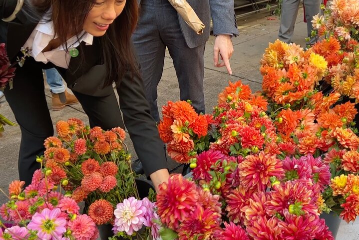 Warm toned flowers in buckets for sale on sidewalk, people pointing
